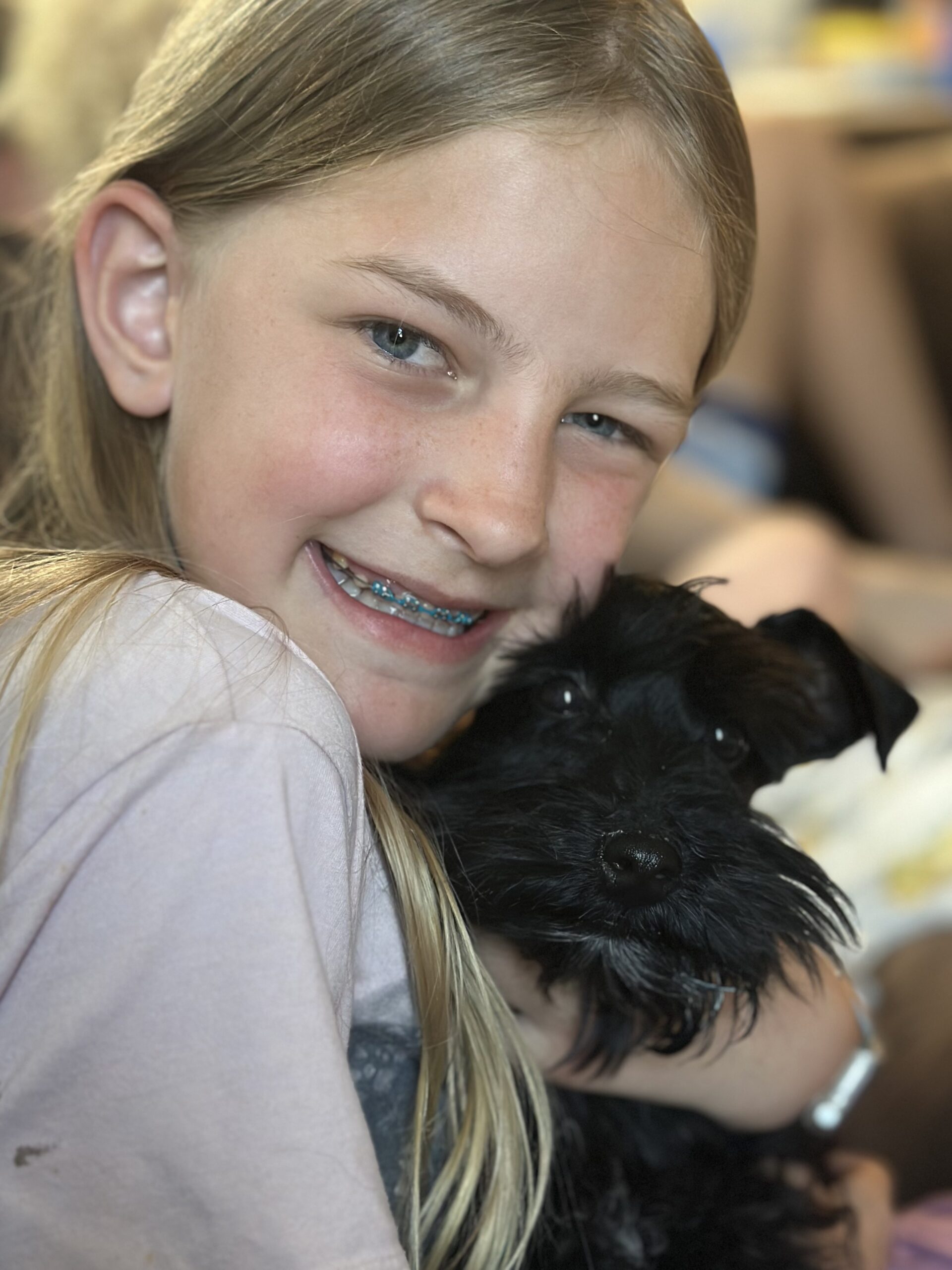 Smiling girl with braces hugs a small black dog, showcasing a joyful bond between pets and children. This image highlights companionship.